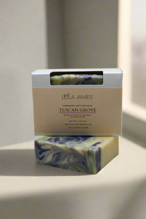 Bar of soap with green, purple, and white marbled design and packaging labeled 'Lola James' on a white background